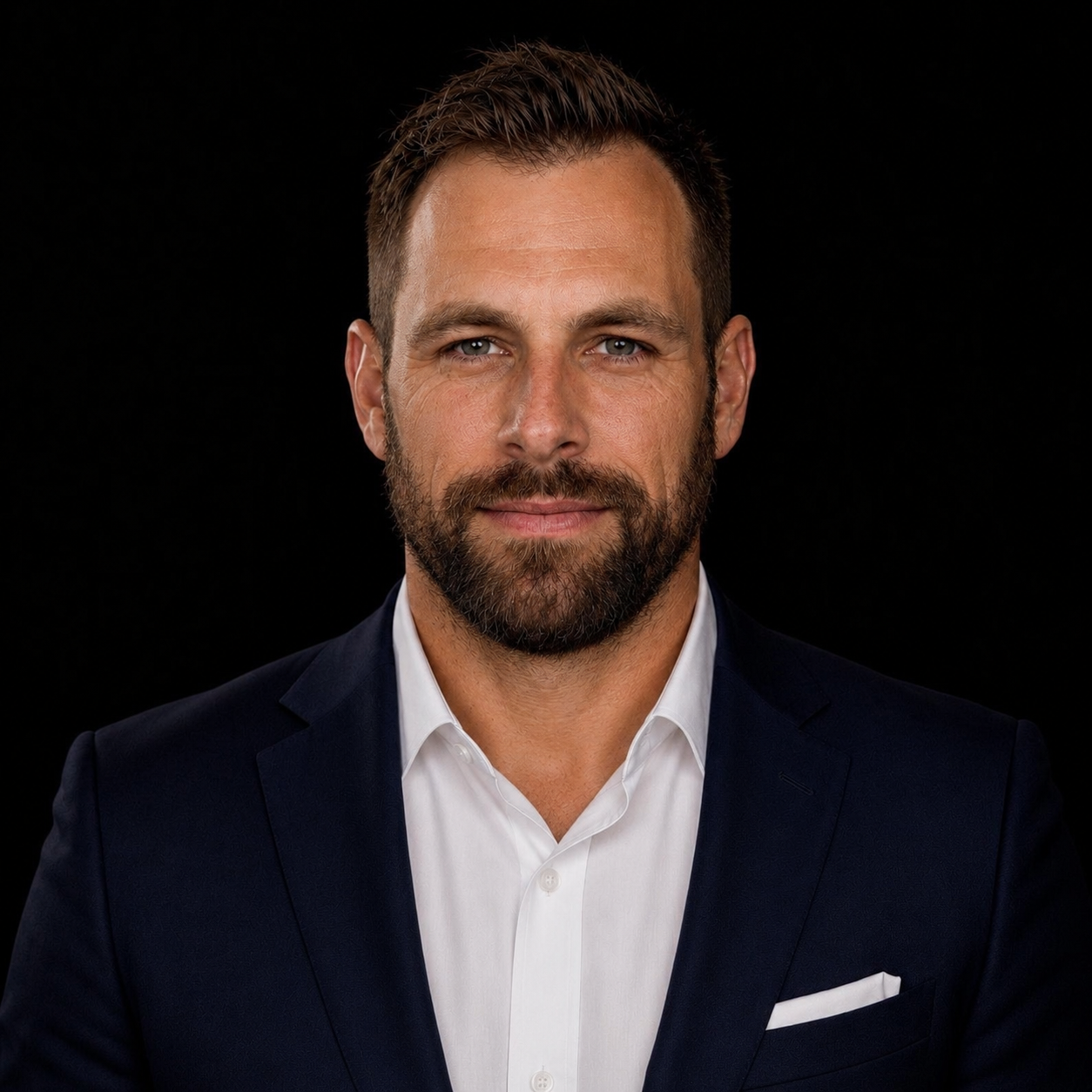 Professional headshot of Rory Avant wearing a navy suit jacket and white shirt against a black background.